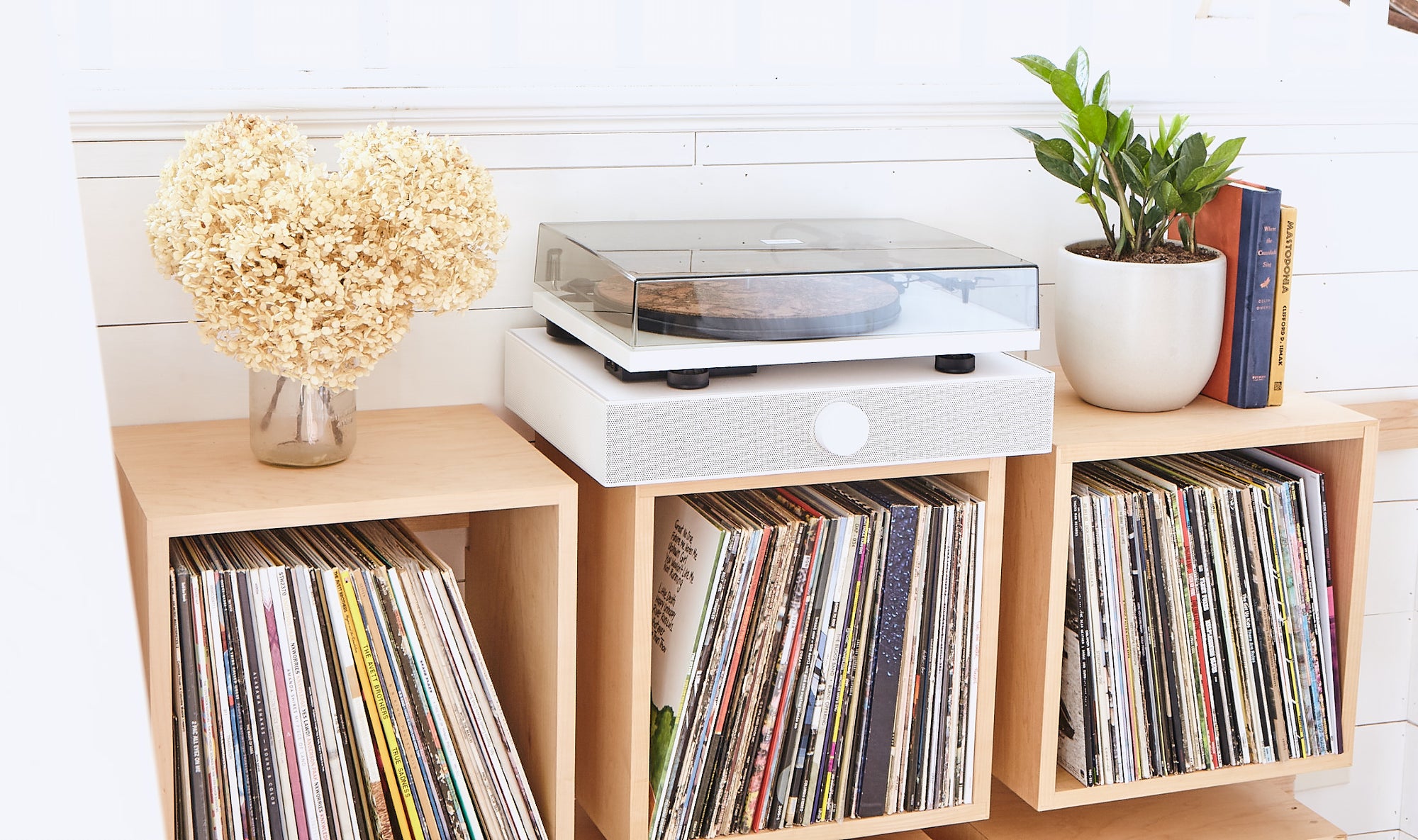 A white Andover SpinDeck turntable on top of a white SpinBase speaker system sitting on maple Wall Cube record shelves