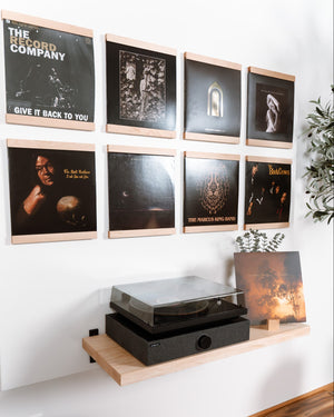 A styled interior wall showing a wall-mounted maple hardwood shelf that frames a vinyl record on the top and bottom. Eight units are organized in a grid above a record player on a matching maple hardwood floating table top. Because a real room environment is visible, this is Lifestyle rather than Product/Packaging.