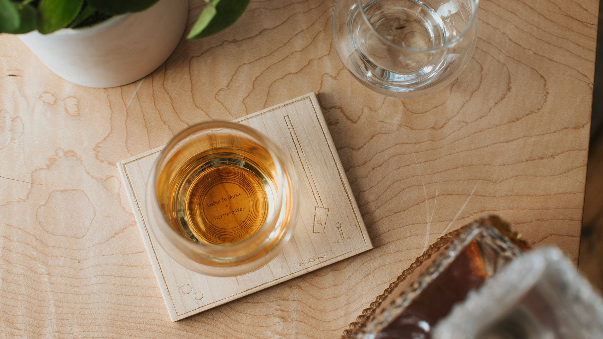 A glass of whisky sitting on a turntable coaster made out of wood next to a decanter