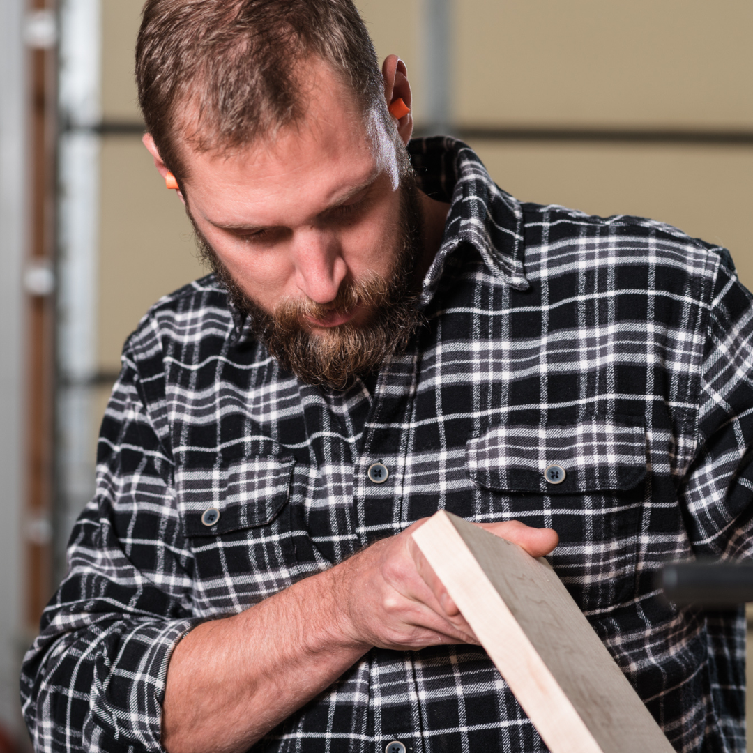 A man in a woodshop looking at lumber before working on it to make handmade record shelving